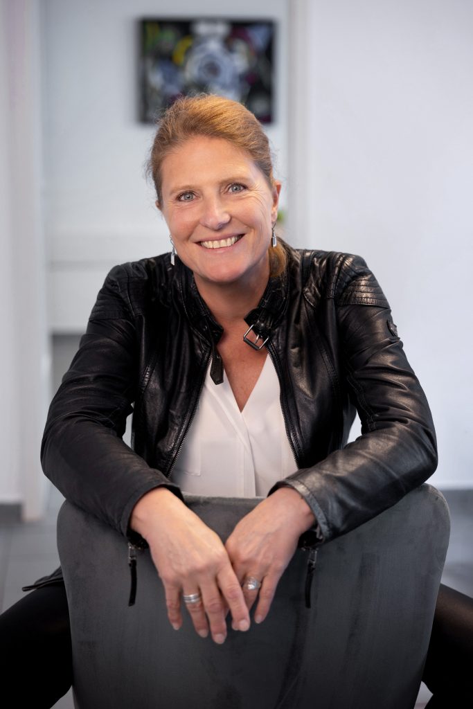 Foto von Steuerberaterin Stefanie Dumitresu die auf einem Stuhl sitzt und in die Kamera lächelt.